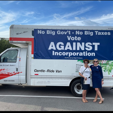 Linda Nelson with another woman standing in front of a moving truck with a large sign against incorporating The Woodlands